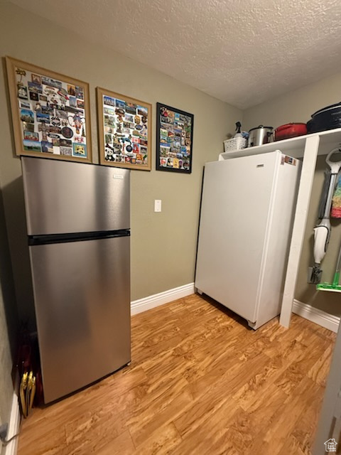Kitchen with freestanding refrigerator, light wood-style flooring, and a textured ceiling