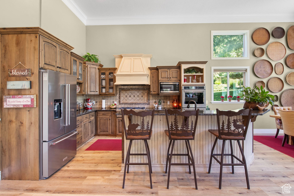 Kitchen with appliances with stainless steel finishes, light wood finished floors, ornamental molding, a breakfast bar area, and decorative backsplash