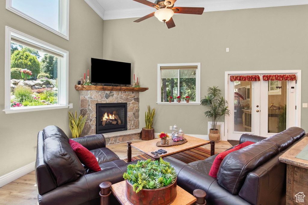 Living room with wood finished floors, crown molding, a ceiling fan, a towering ceiling, and a fireplace