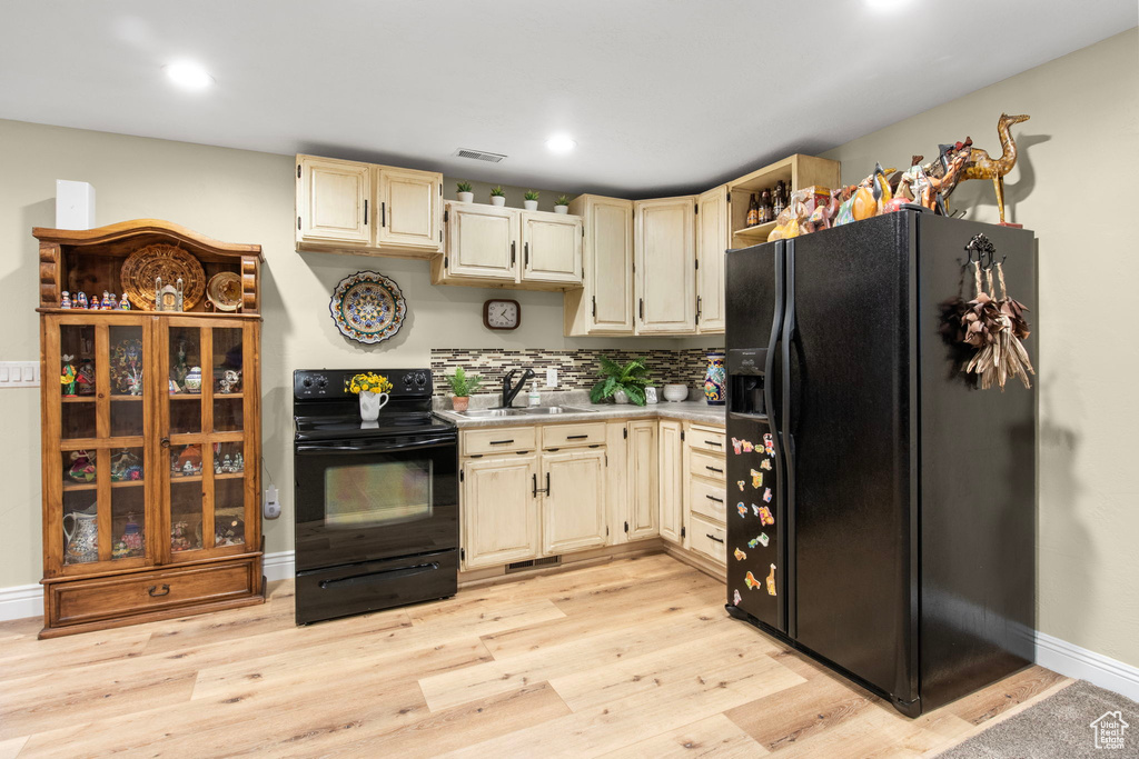 Kitchen featuring black appliances, light countertops, light wood-style flooring, cream cabinetry, and recessed lighting