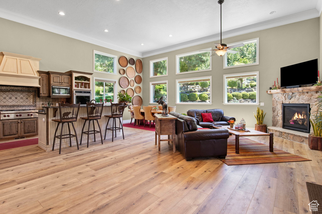 Living area featuring ornamental molding, a stone fireplace, a high ceiling, a ceiling fan, and healthy amount of natural light