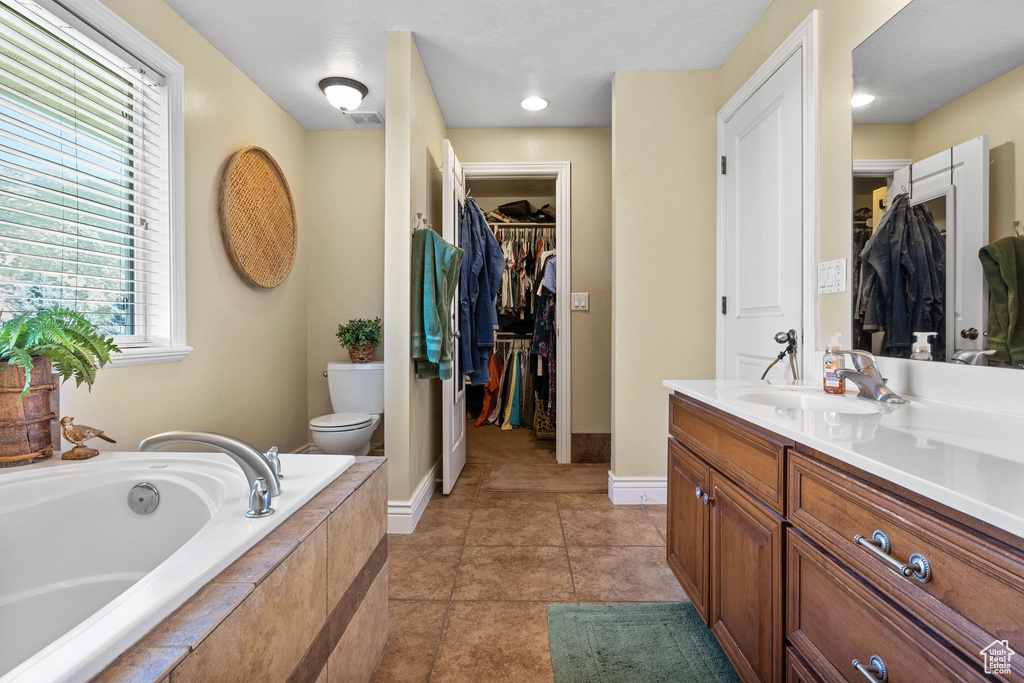 Bathroom with vanity, a bath, a walk in closet, and tile patterned flooring