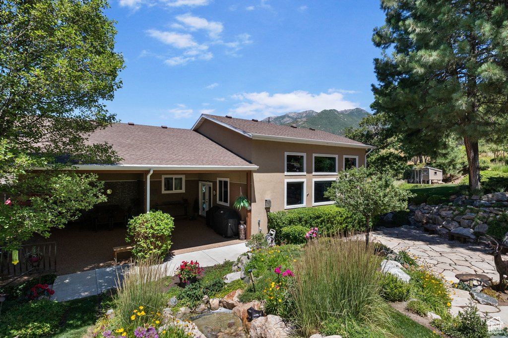 Rear view of house featuring stucco siding, a shingled roof, a mountain view, and a patio area