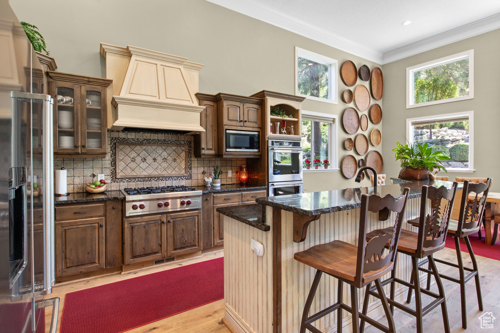 Kitchen with stainless steel appliances, a breakfast bar, light wood finished floors, crown molding, and decorative backsplash