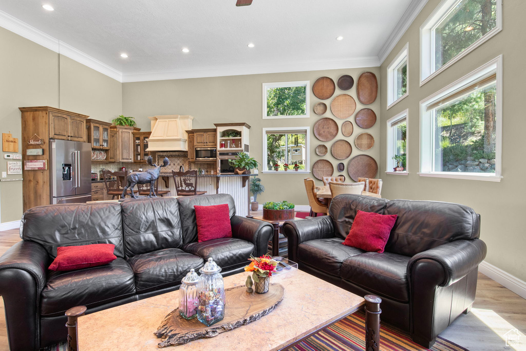 Living area featuring a high ceiling, crown molding, light wood-style floors, and recessed lighting