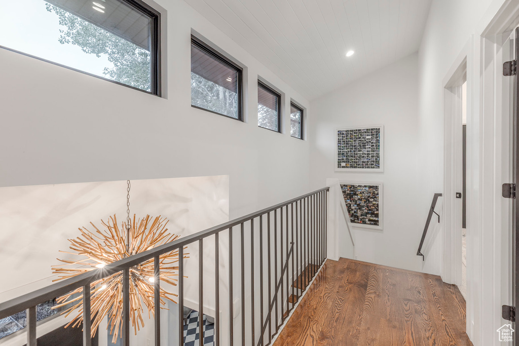 Corridor featuring an upstairs landing, a chandelier, wood finished floors, healthy amount of natural light, and lofted ceiling