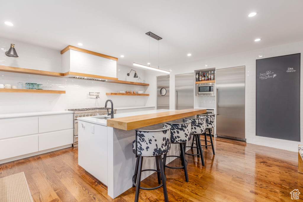 Kitchen with open shelves, modern cabinets, white cabinetry, built in appliances, and light wood finished floors
