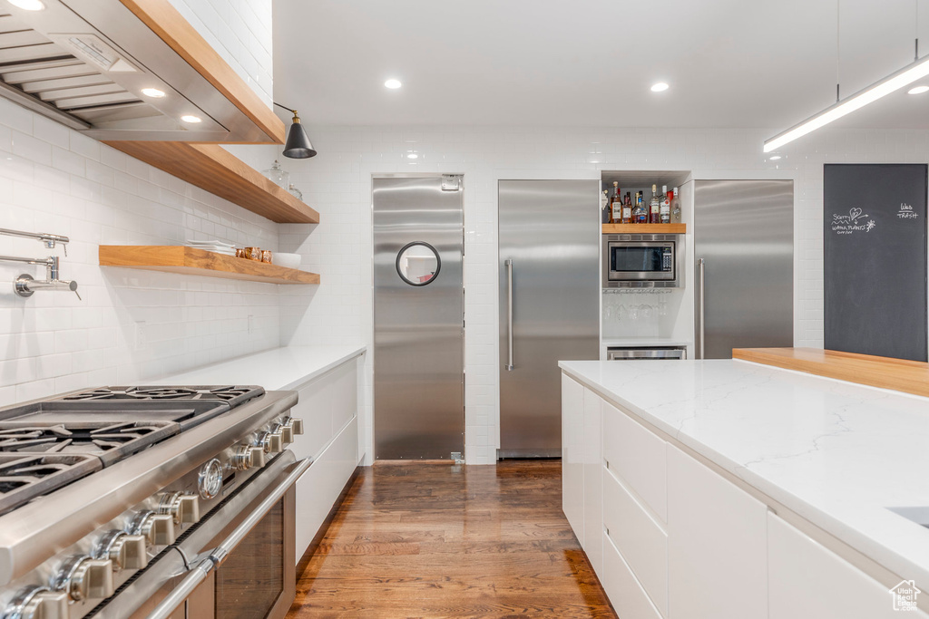 Kitchen featuring open shelves, built in appliances, extractor fan, white cabinetry, and wood finished floors
