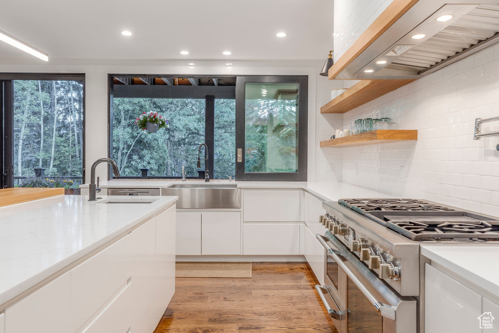 Kitchen featuring range with two ovens, white cabinets, recessed lighting, wall chimney exhaust hood, and decorative backsplash