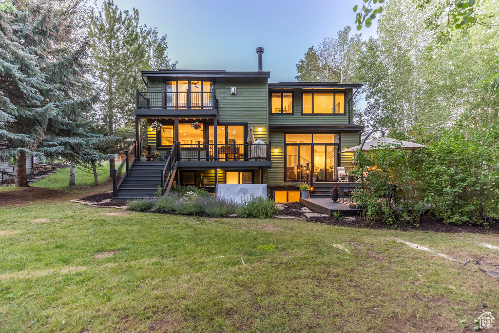 Rear view of property with stairs, a wooden deck, a lawn, and a balcony