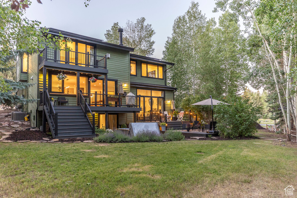 Back of property with a balcony, stairway, a lawn, and a deck