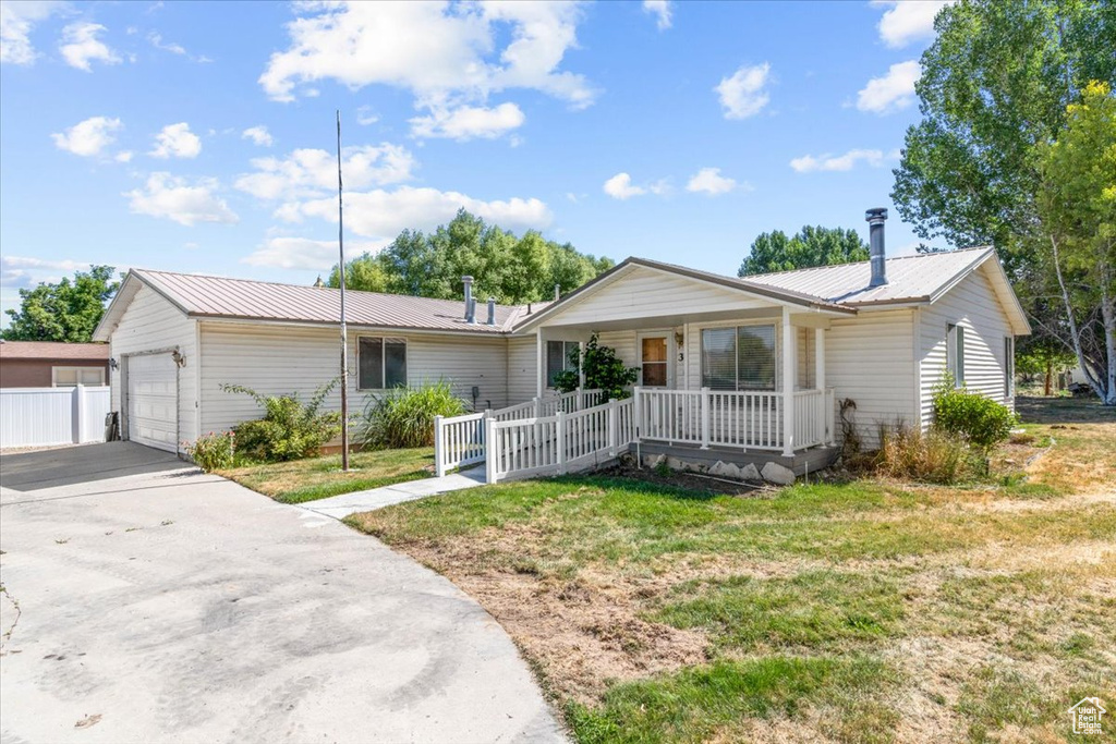 Ranch-style house featuring a porch, a metal roof, concrete driveway, and a front lawn