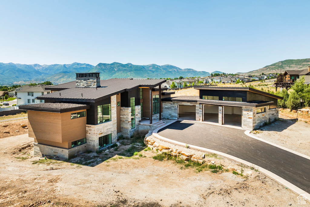 Modern home with a standing seam roof, stone siding, a metal roof, a mountain view, and asphalt driveway