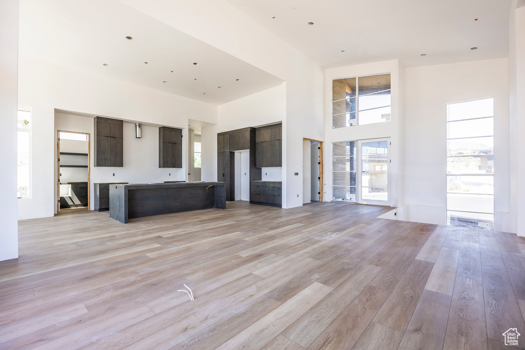 Unfurnished living room featuring light wood finished floors, a towering ceiling, and plenty of natural light