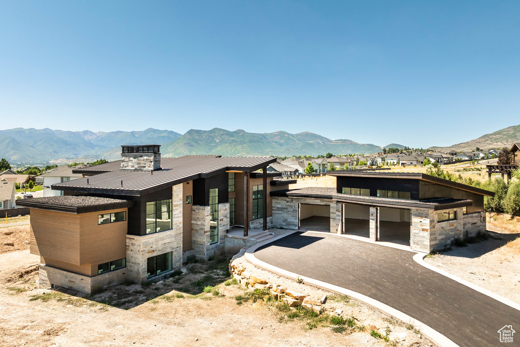 Contemporary home featuring a standing seam roof, stone siding, a metal roof, a mountain view, and asphalt driveway