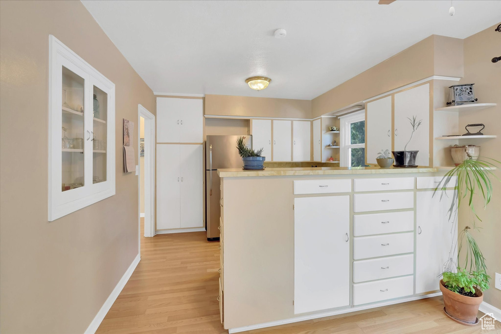 Kitchen featuring open shelves, light wood-style floors, freestanding refrigerator, and white cabinetry