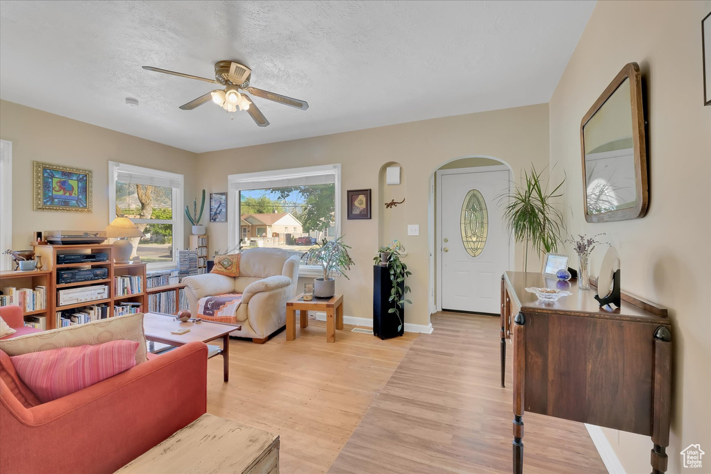 Living area with light wood finished floors, a ceiling fan, and arched walkways
