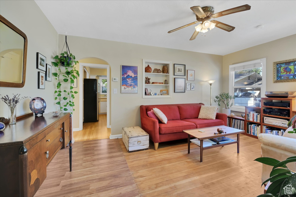 Living room with ceiling fan, light wood-style floors, and arched walkways