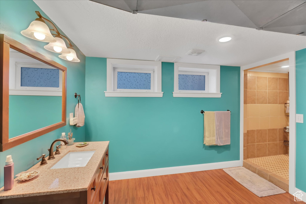 Bathroom with wood finished floors, a tile shower, vanity, and recessed lighting