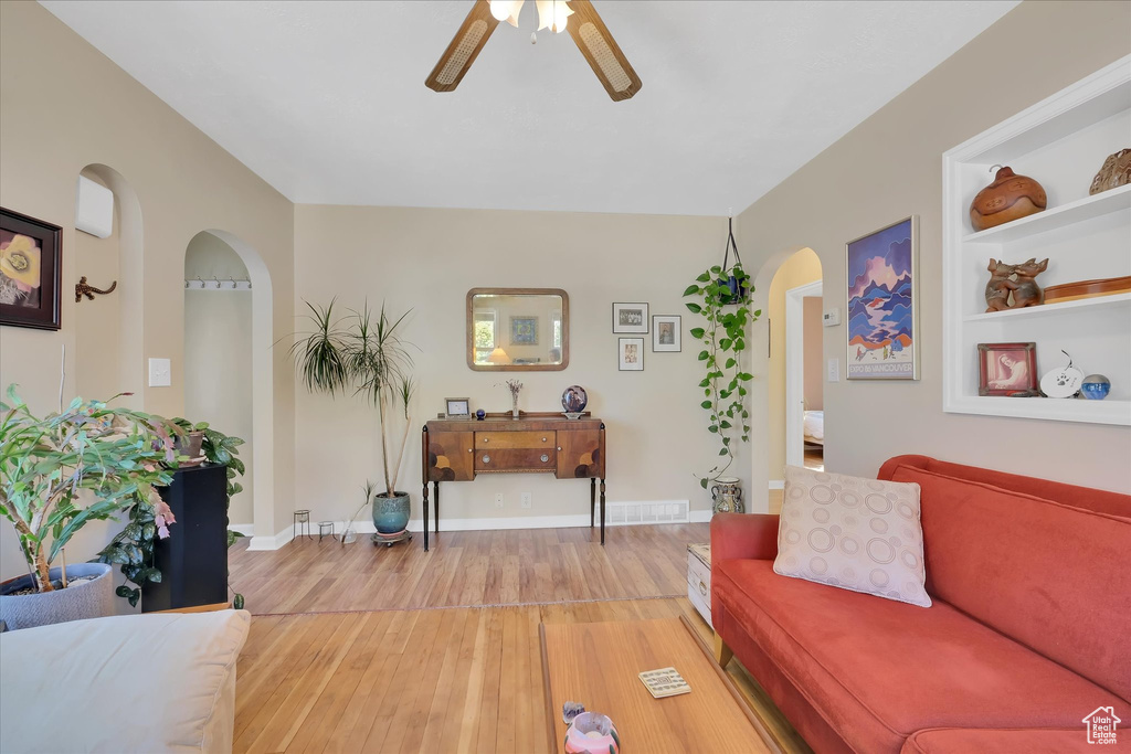 Living area with arched walkways, ceiling fan, and light wood finished floors
