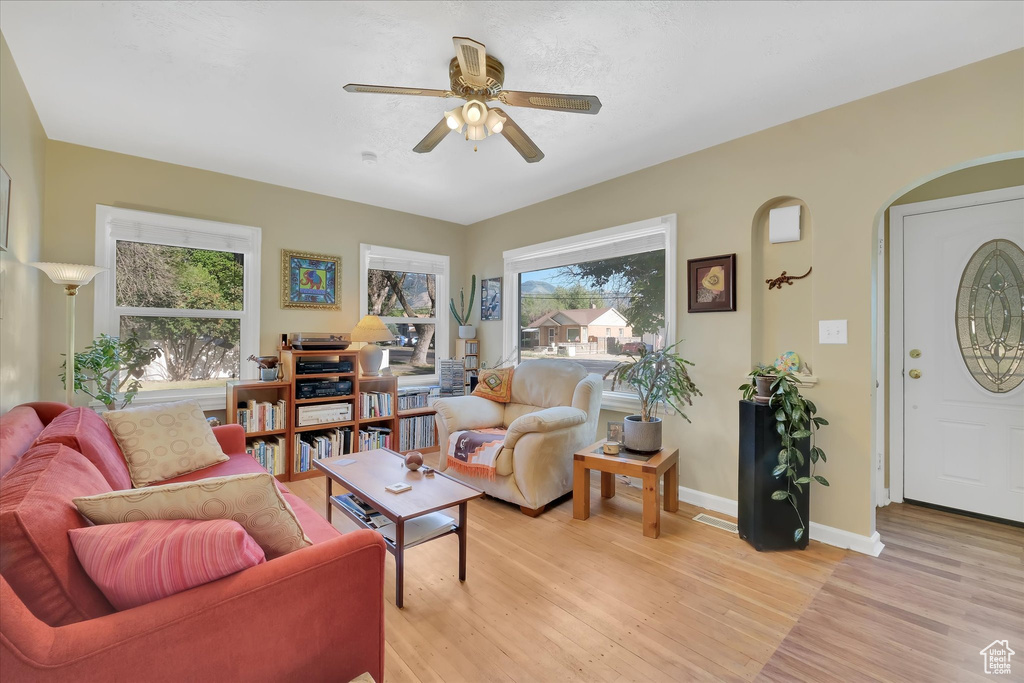 Living room with ceiling fan, light wood-style floors, and arched walkways