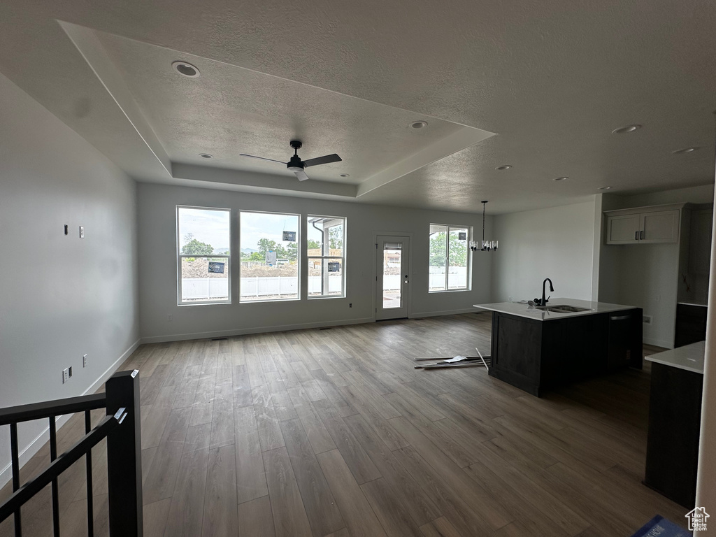 Unfurnished living room with a tray ceiling, ceiling fan, a textured ceiling, wood finished floors, and a chandelier