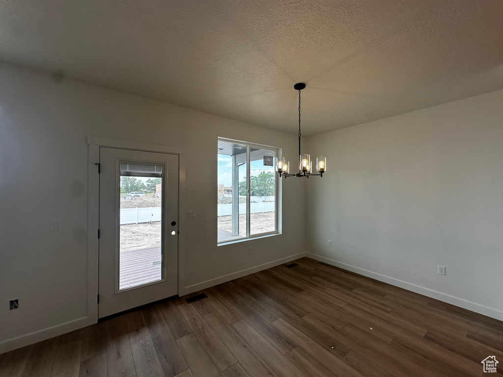 Unfurnished dining area featuring a chandelier, dark wood-style floors, and a textured ceiling