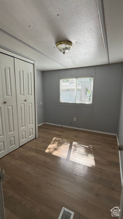 Unfurnished bedroom with wood-type flooring, a textured ceiling, and a closet