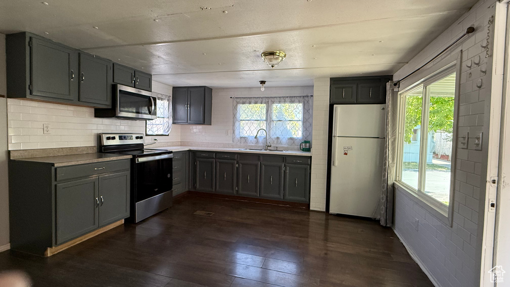 Kitchen with stainless steel appliances, decorative backsplash, dark wood-style flooring, and gray cabinetry