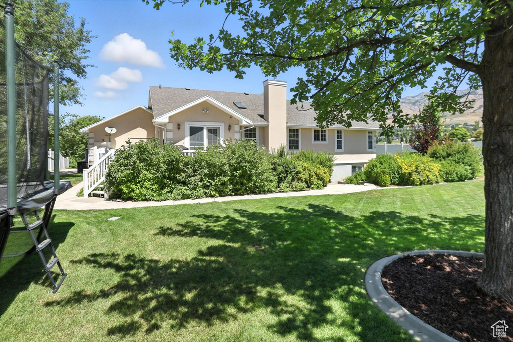 View of front facade with stucco siding, a chimney, a front lawn, a trampoline, and stairs