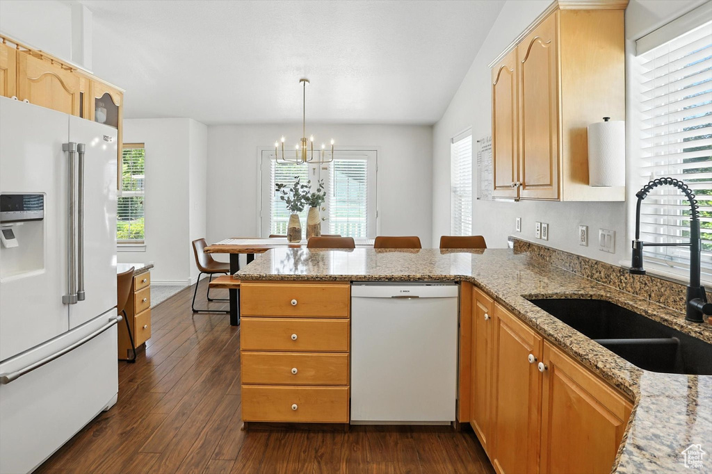 Kitchen with white appliances, a chandelier, a peninsula, dark wood-type flooring, and light stone counters