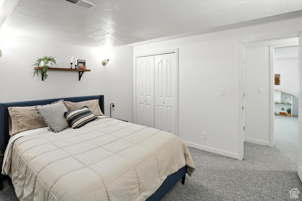Carpeted bedroom featuring a textured ceiling and a closet