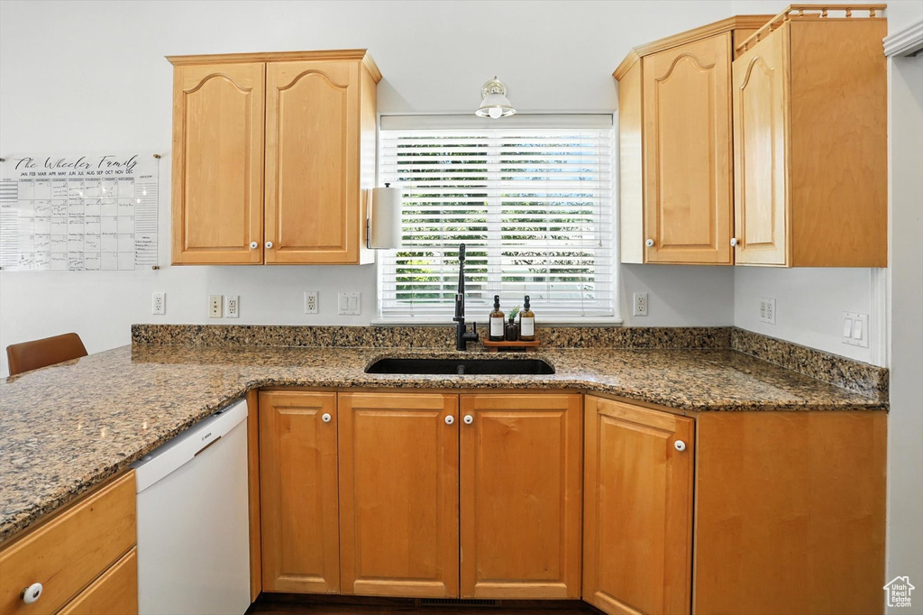 Kitchen with dishwasher, dark stone countertops, and light brown cabinets