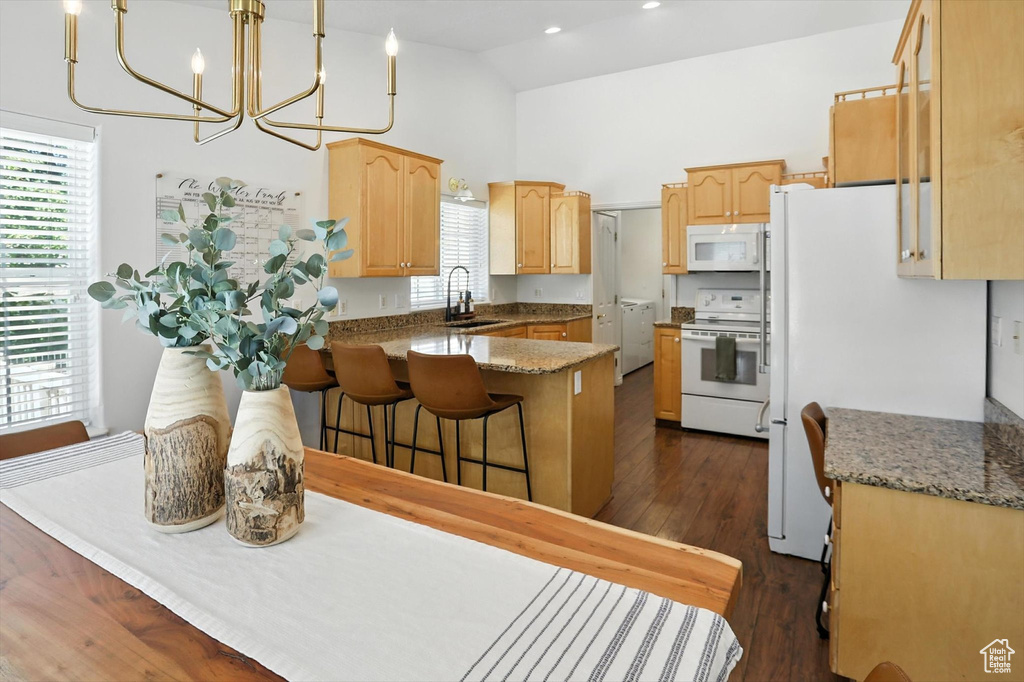 Kitchen featuring a peninsula, white appliances, light brown cabinets, high vaulted ceiling, and a chandelier