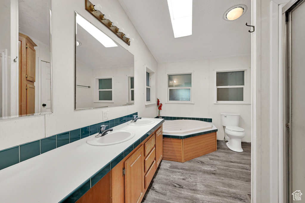 Full bath with double vanity, a bath, wood finished floors, and a skylight
