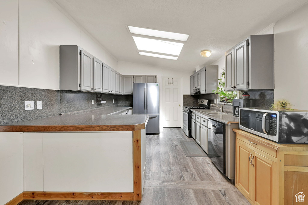 Kitchen with lofted ceiling, stainless steel appliances, light wood-style flooring, decorative backsplash, and a peninsula