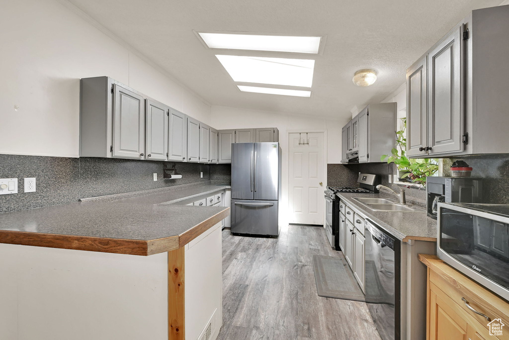 Kitchen with appliances with stainless steel finishes, backsplash, vaulted ceiling, light wood-style flooring, and a peninsula