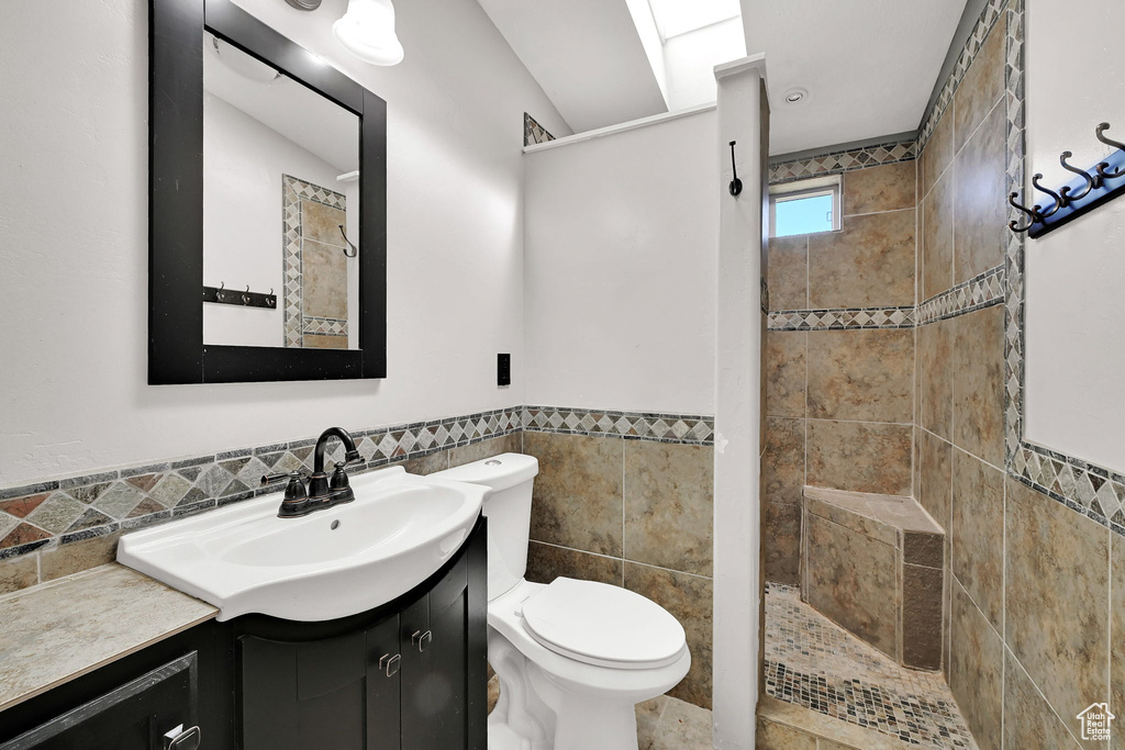 Bathroom featuring tile walls, vanity, a tile shower, and a wainscoted wall