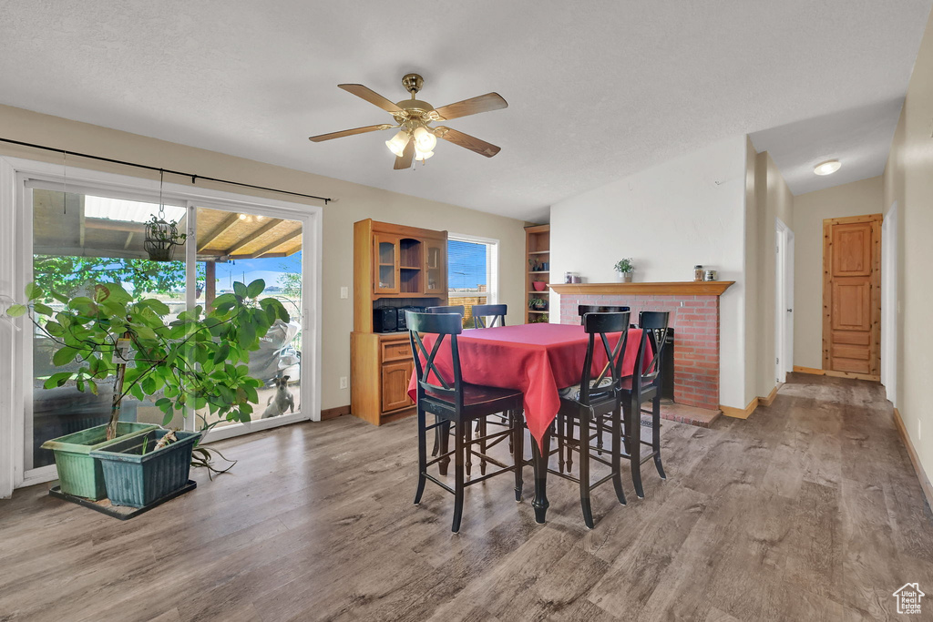 Dining room featuring light wood finished floors, ceiling fan, and a brick fireplace