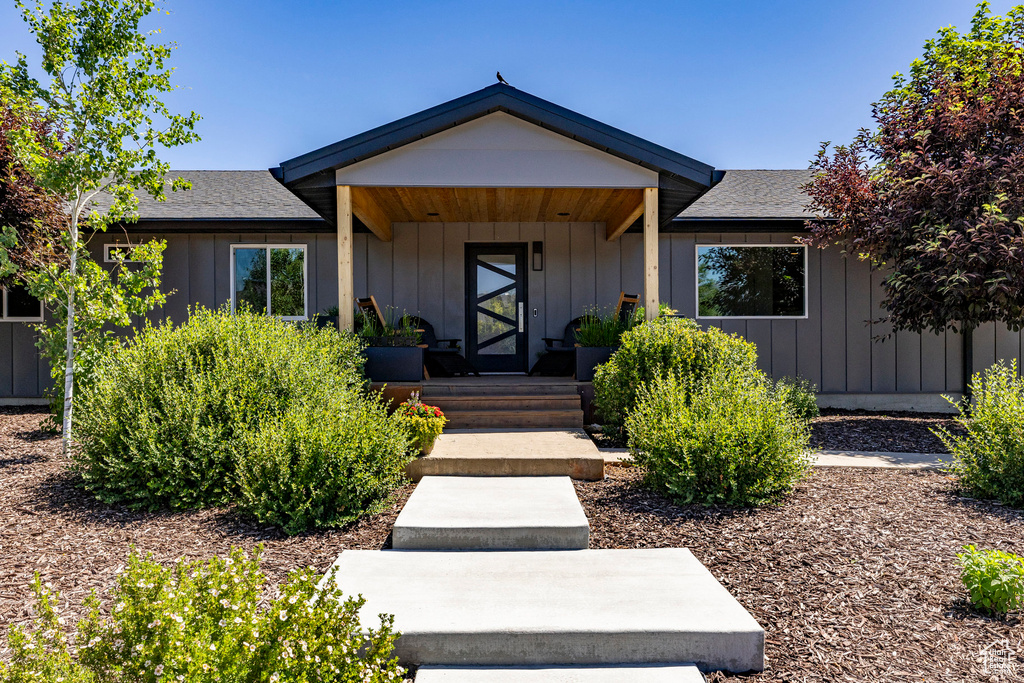 View of exterior entry featuring roof with shingles, board and batten siding, and a porch
