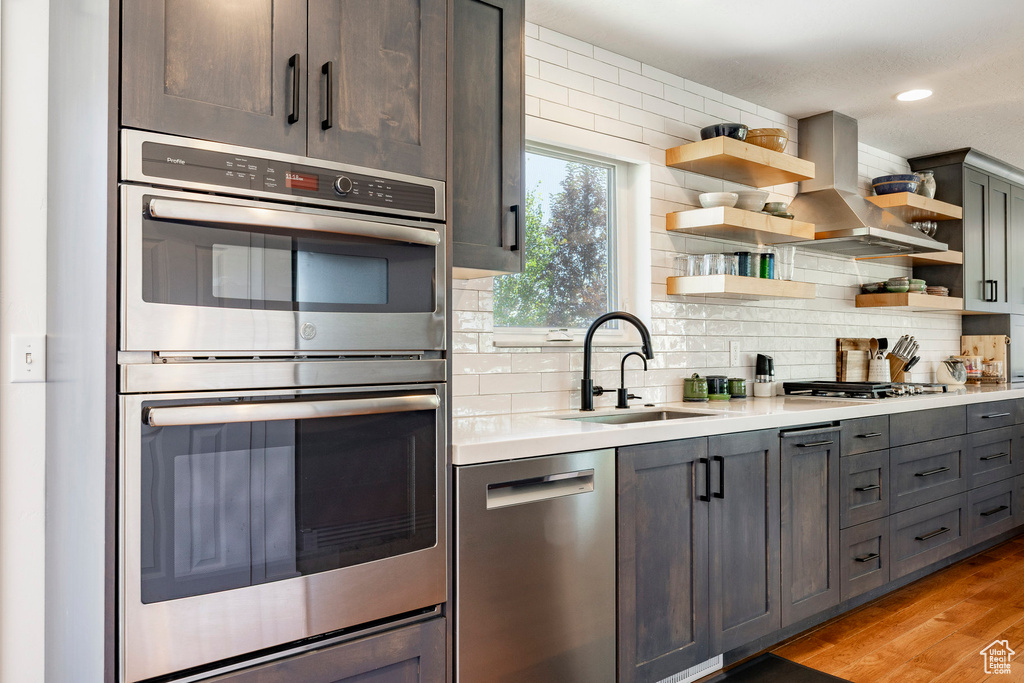 Kitchen featuring stainless steel appliances, open shelves, light countertops, decorative backsplash, and island range hood