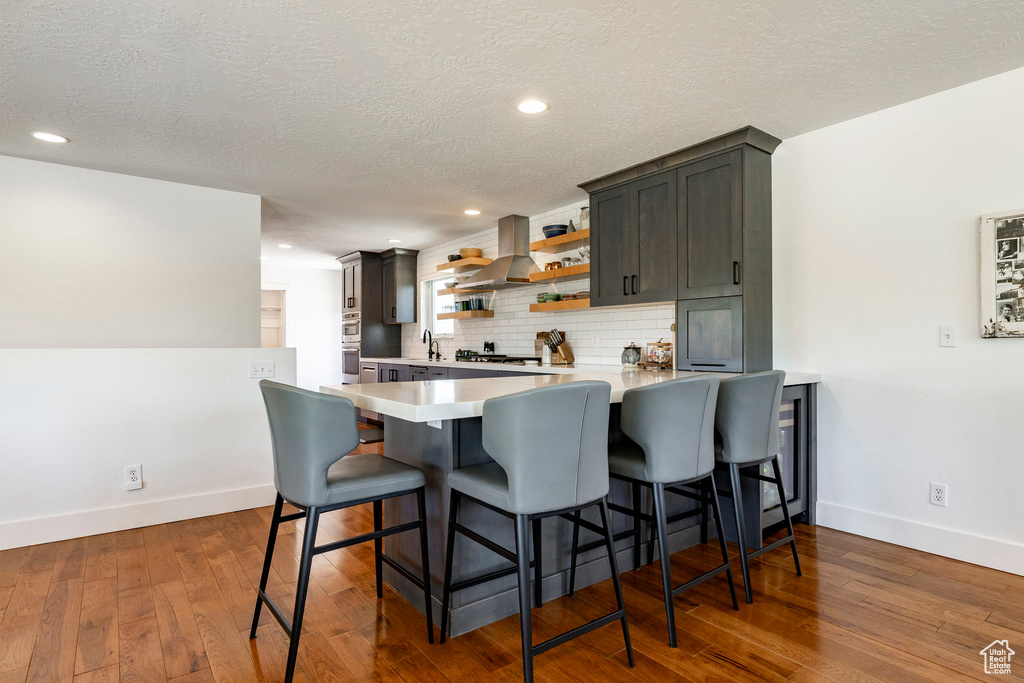 Kitchen featuring light countertops, tasteful backsplash, a peninsula, open shelves, and hardwood / wood-style flooring