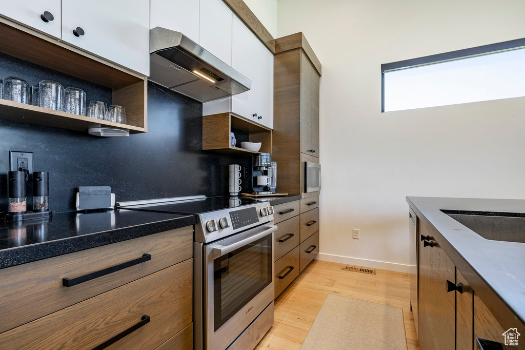 Kitchen featuring stainless steel appliances, open shelves, wall chimney exhaust hood, and light wood-style floors