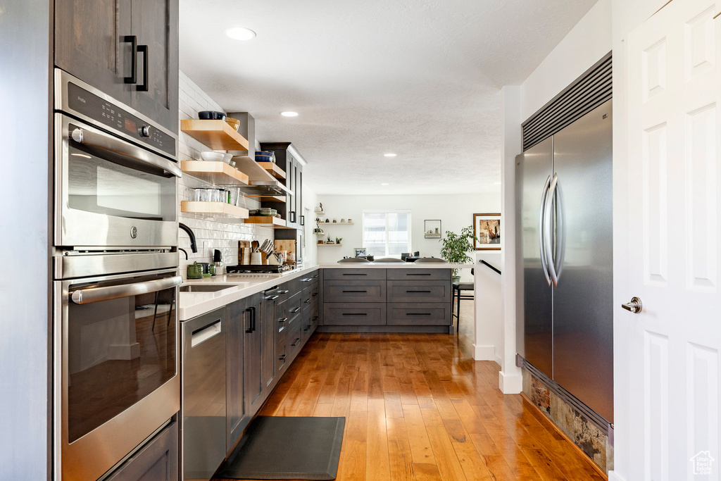 Kitchen with open shelves, appliances with stainless steel finishes, gray cabinets, light wood-style flooring, and light countertops