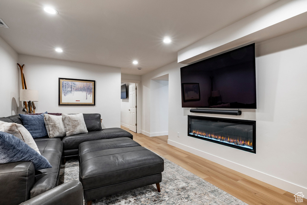 Living room with a glass covered fireplace, recessed lighting, and light wood-style flooring
