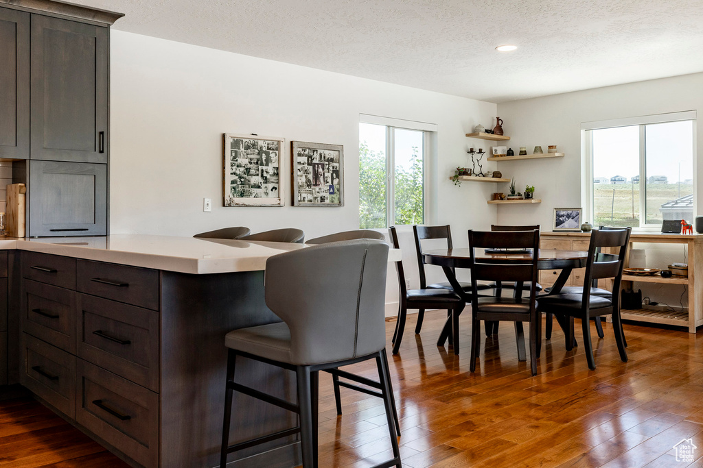 Kitchen with a kitchen bar, healthy amount of natural light, dark brown cabinetry, light countertops, and a textured ceiling