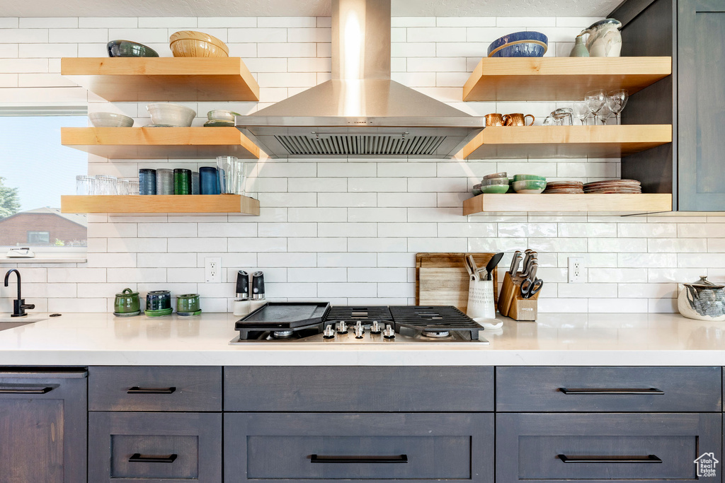 Kitchen featuring open shelves, gray cabinets, wall chimney range hood, and backsplash