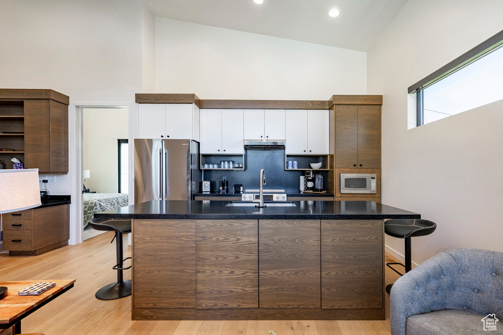 Kitchen with high vaulted ceiling, open shelves, a kitchen bar, freestanding refrigerator, and white cabinets