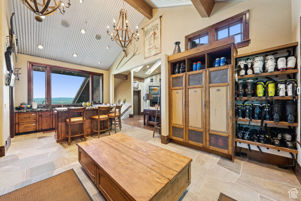 Living room with a chandelier, high vaulted ceiling, beamed ceiling, and stone tile flooring