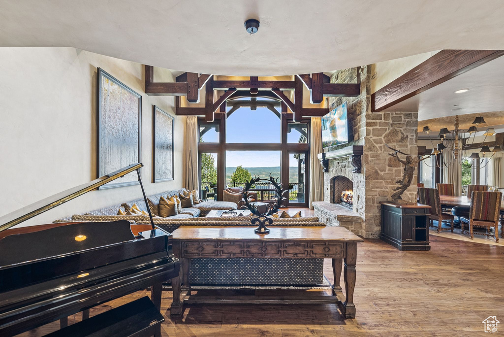 Living room with wood finished floors, healthy amount of natural light, a stone fireplace, and beam ceiling